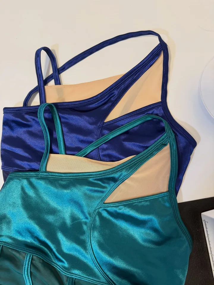 Three navy and teal dance costume tops with added beige power-mesh panels, laid on a worktable.